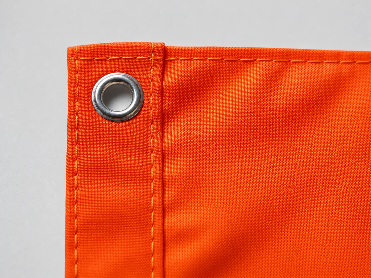 Close-up of a metal grommet and reinforced stitching on an orange custom flag